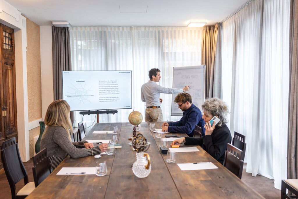 Sala meeting di Villa Carona Hotel & Spa attrezzata per riunioni aziendali, con tavolo in legno, schermo multimediale e luce naturale.