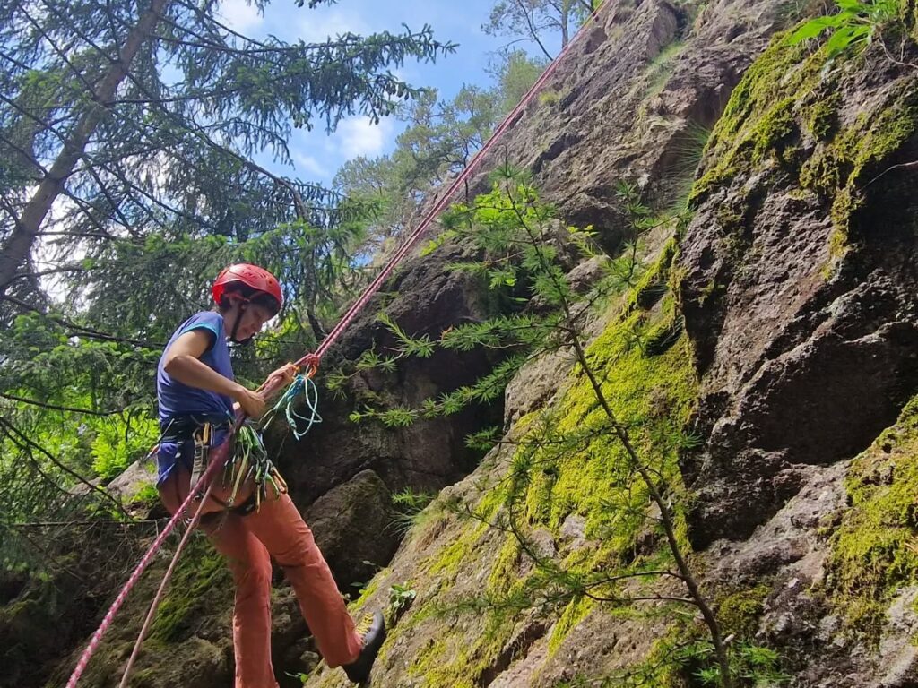 Ragazza che scala una parete rocciosa tra i boschi della Val Brembana, con imbrago e casco
