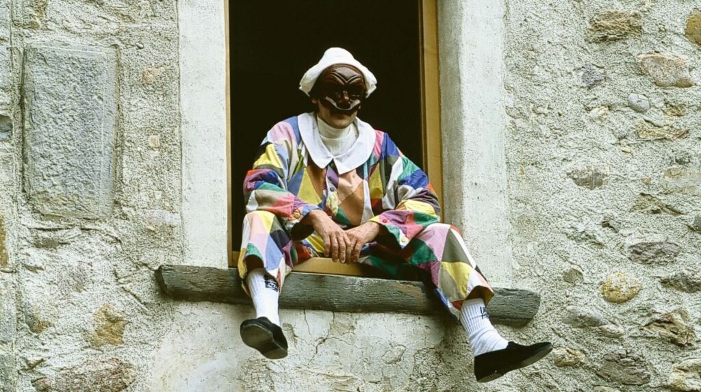 Attore in costume di Arlecchino alla finestra della Casa Museo a Oneta, borgo storico in Val Brembana