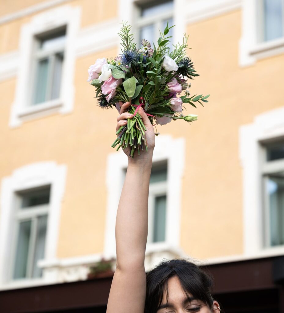 Dettaglio di una sposa che alza il bouquet davanti alla facciata dell’hotel Villa Carona